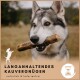 Ein wolfähnlicher Hund hält einen Kauartikel, mit einem verschwommenen Hintergrund im Freien und dem Text: "LANGANHALTENDES KAUVERGNÜGEN" und "natürlich & kalorienfrei."