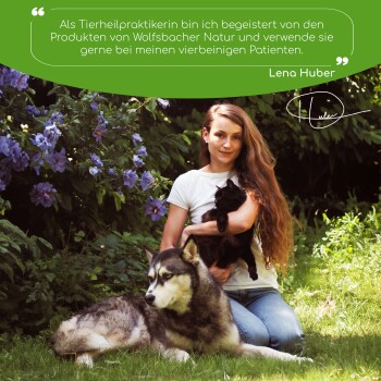Eine Frau mit einer schwarzen Katze und einem Wolfhund in üppigem Grün, mit einem Testimonial von Lena Huber über Wolfsbacher Natur-Tierprodukte.