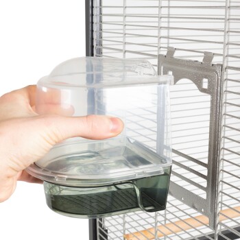 Eine Hand hält eine klare Plastik-Wasserflasche, die für einen Haustierkäfig entworfen wurde, positioniert in der Nähe des Metallrahmens des Käfigs mit Drahtgittern.