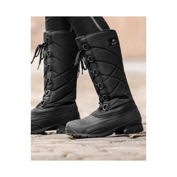 Schwarze isolierte Winterstiefel mit einem gesteppten Design und Schnürsenkeln, getragen von einer Person, die auf einer Kopfsteinpflasteroberfläche steht.