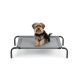 Ein kleiner, flauschiger Hund sitzt auf einem grauen erhöhten Haustierbett mit schwarzen Metallbeinen und zeigt einen komfortablen Ruheplatz.